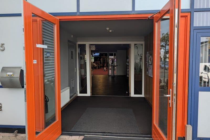 De oranje deuren van Het Lichtbaken staan wijd open. Door de hal kijk je de zaal in.